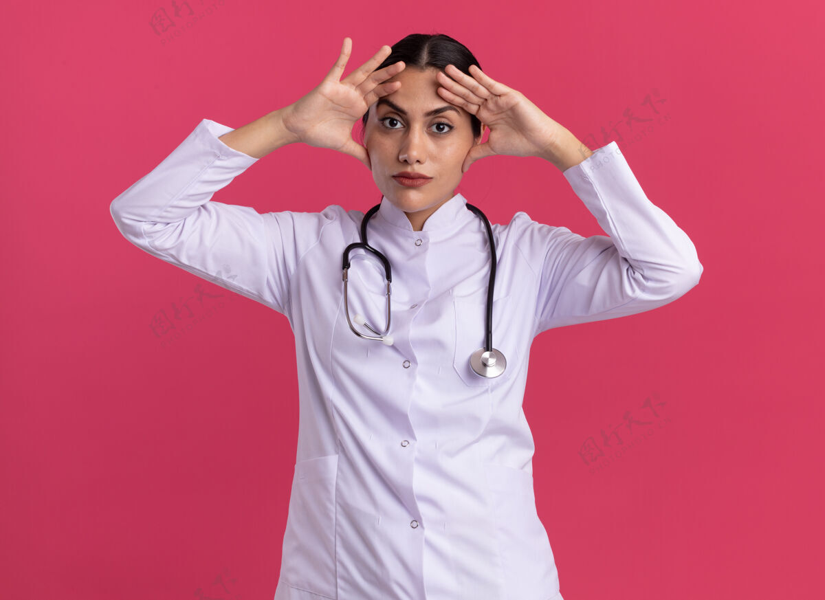 年轻年轻的女医生 穿着医用外套 站在粉红色的墙上 带着听诊器 看上去又累又无聊女人累听诊器