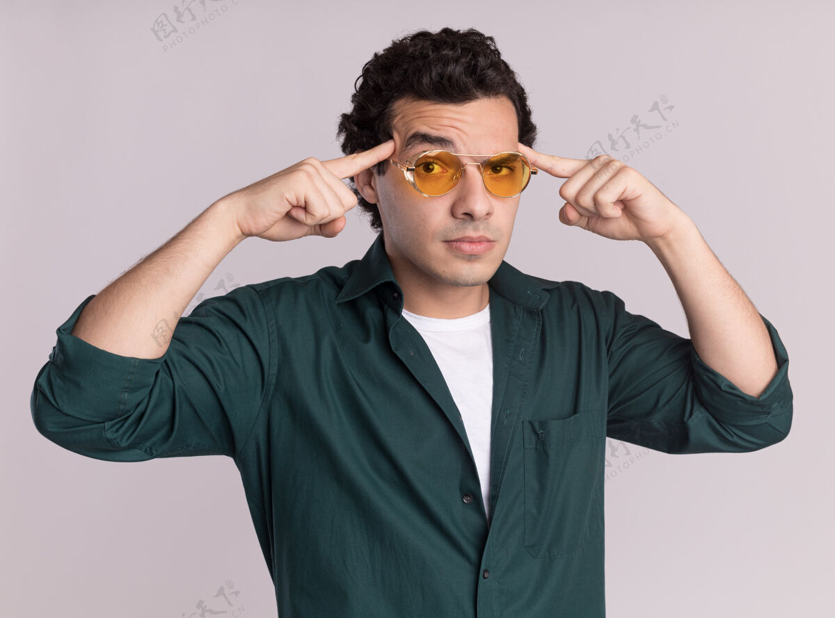 表情穿绿衬衫的年轻人戴着眼镜看着前面 一脸自信的表情 用食指指着他站在白墙上的太阳穴目录指着衬衫