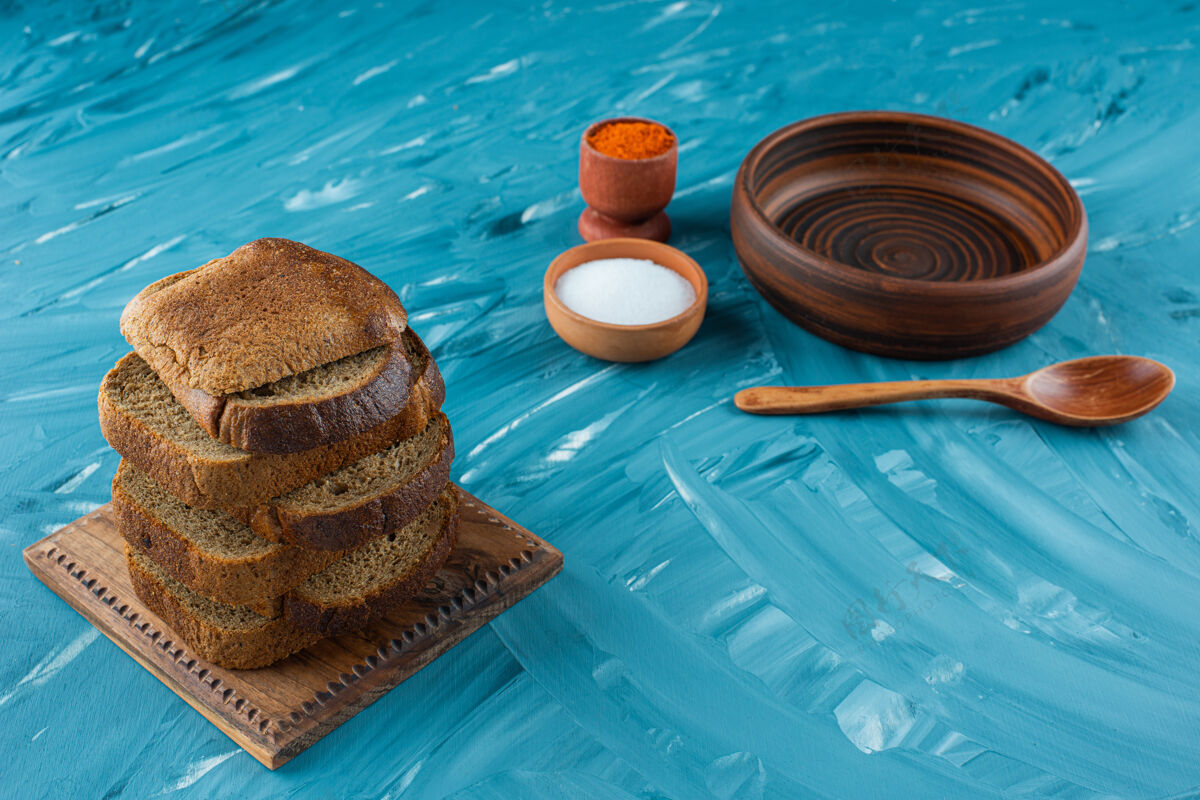 烘焙用盐和蓝色背景的空木勺切的棕色面包面包勺子盐