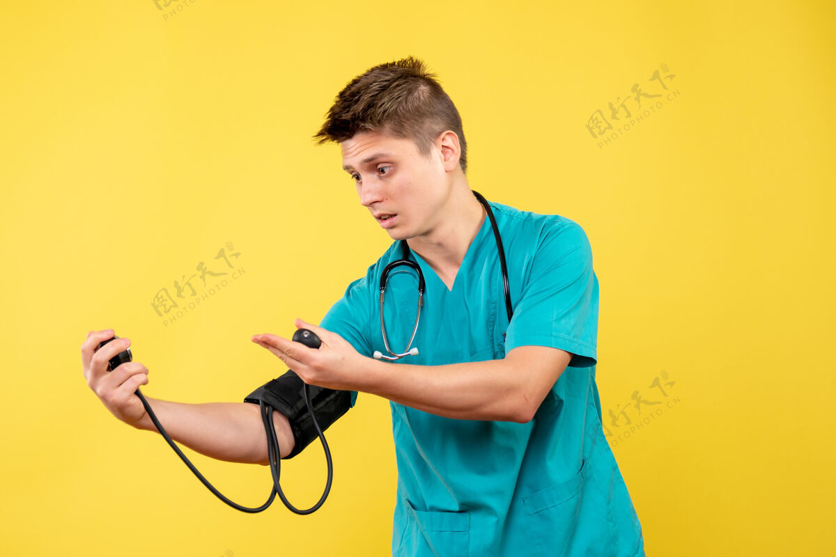 男医生穿着医疗服的男医生在黄色墙壁上检查压力的前视图套装检查医疗仪器