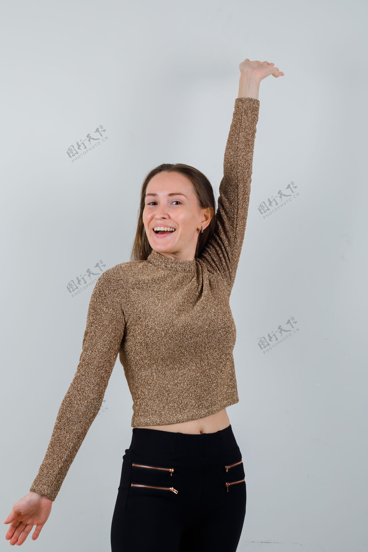 人一个穿着金色金边毛衣和黑色裤子的年轻女子举起手臂 欢欣鼓舞 看上去很幸福肖像漂亮自然