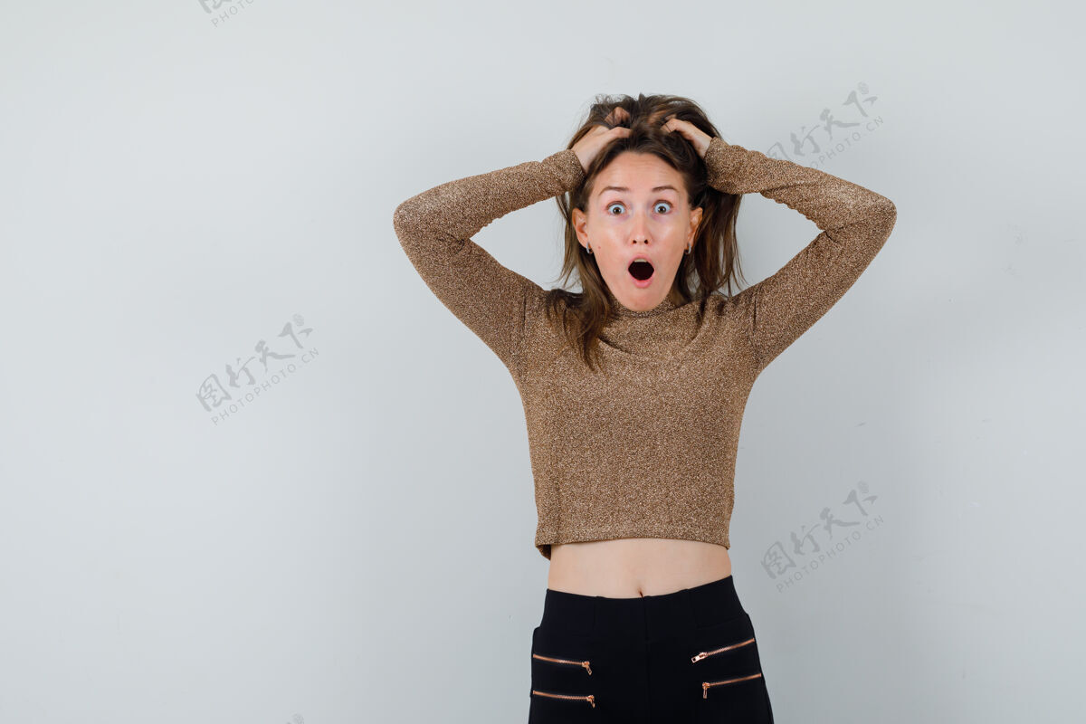 快乐一个年轻的女人 手放在头上 穿着金色的毛衣和黑色的裤子 看起来很惊讶可爱毛衣前面