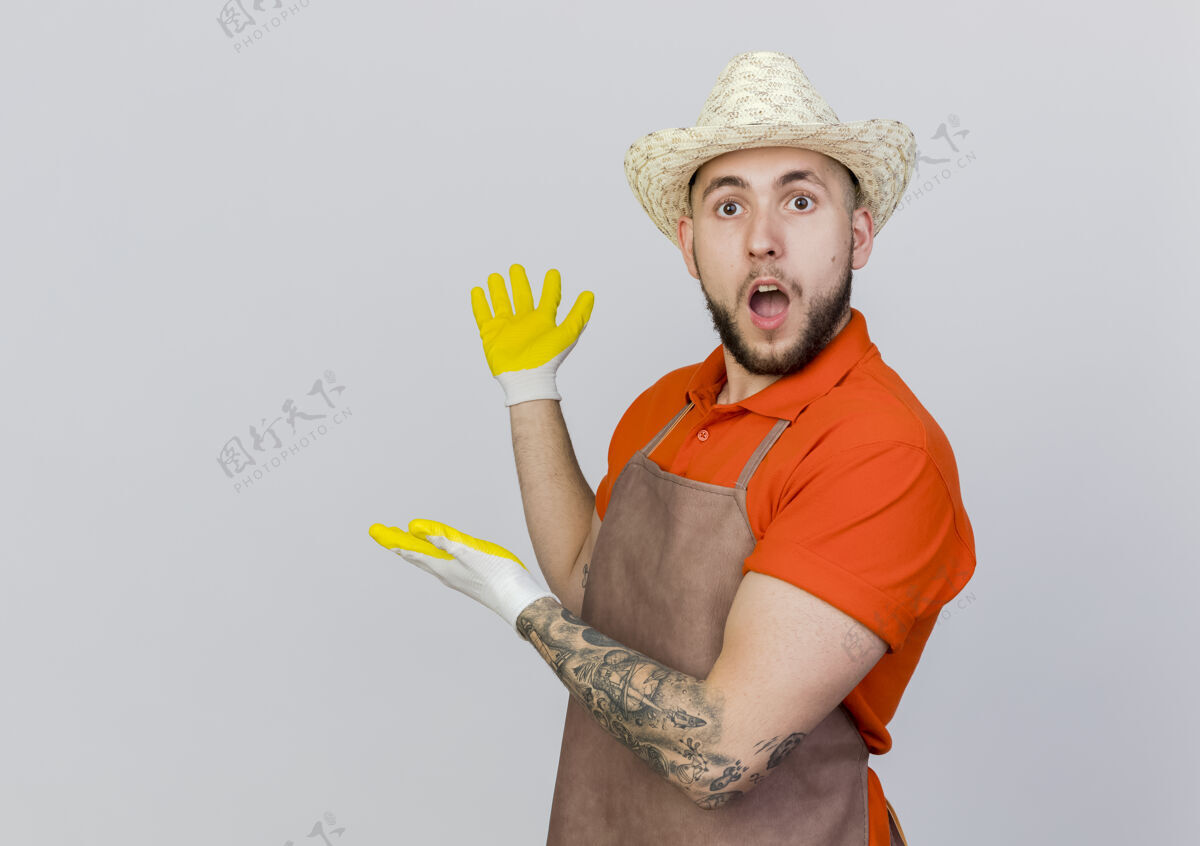 手震惊的男园丁戴着园艺帽和手套 用手指着后面帽子点穿