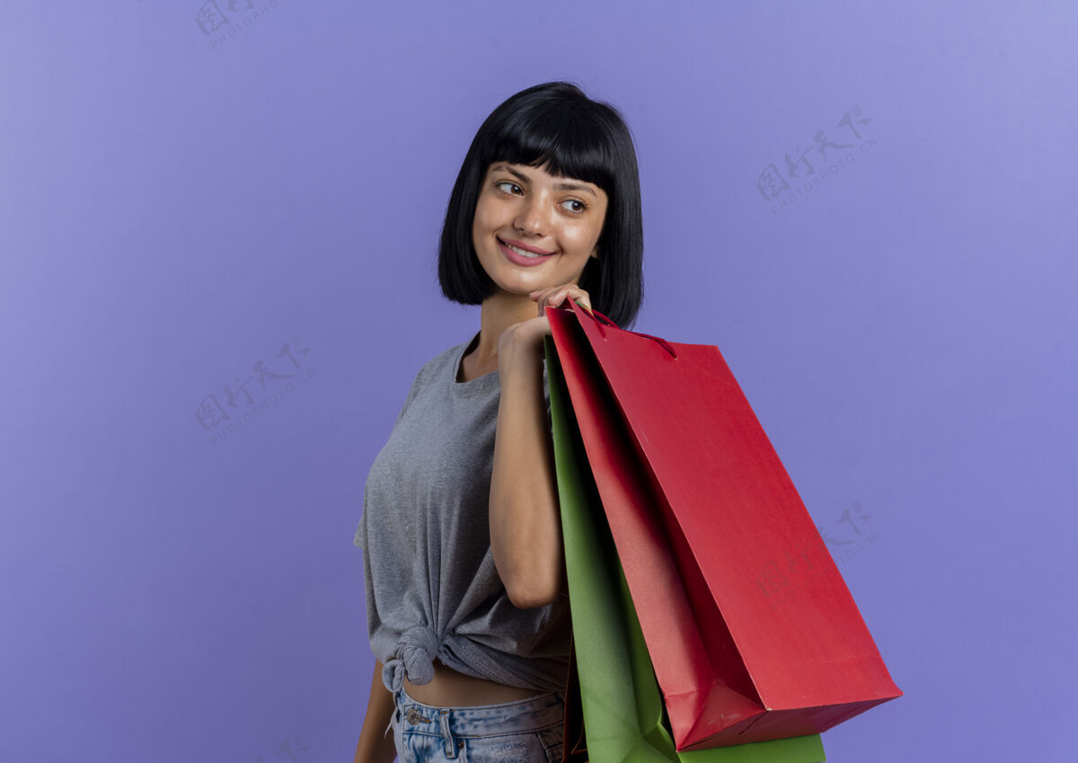 深色微笑着的年轻黑发白人女孩站在一边 肩上扛着五颜六色的购物袋 看着身边空间购物肩膀