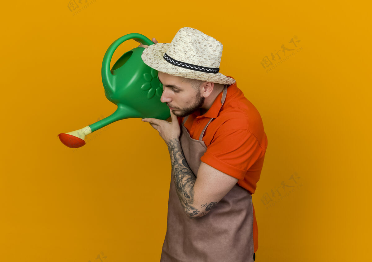 男人年轻的园丁戴着园艺帽站在一边拿着浇水罐往下看橙色拿着放下