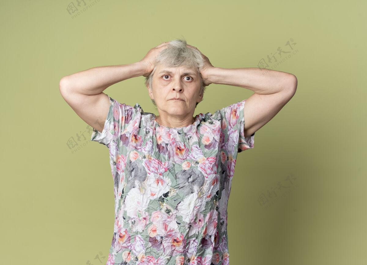 橄榄的震惊的老妇人把头孤立地放在橄榄绿的墙上拿着老的女人