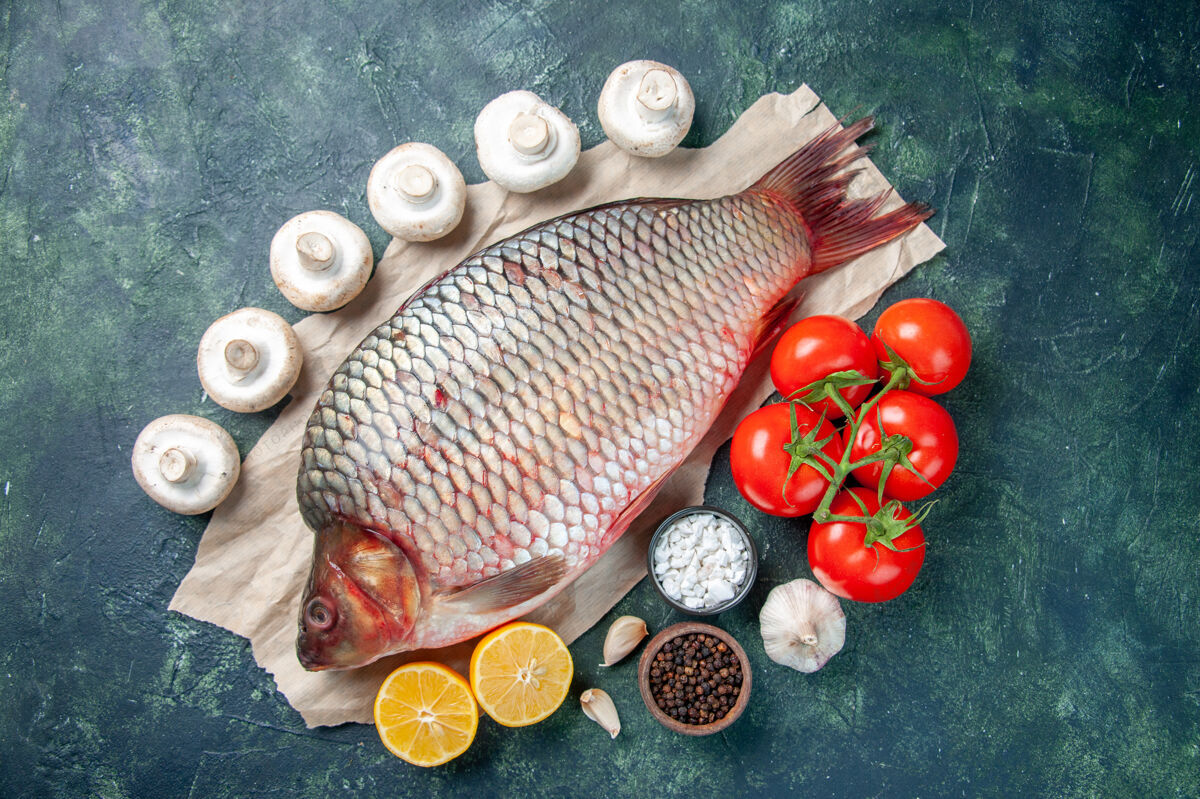 海鲜顶视图新鲜生鱼片与红色西红柿和柠檬片在深蓝色的背景膳食红色景观