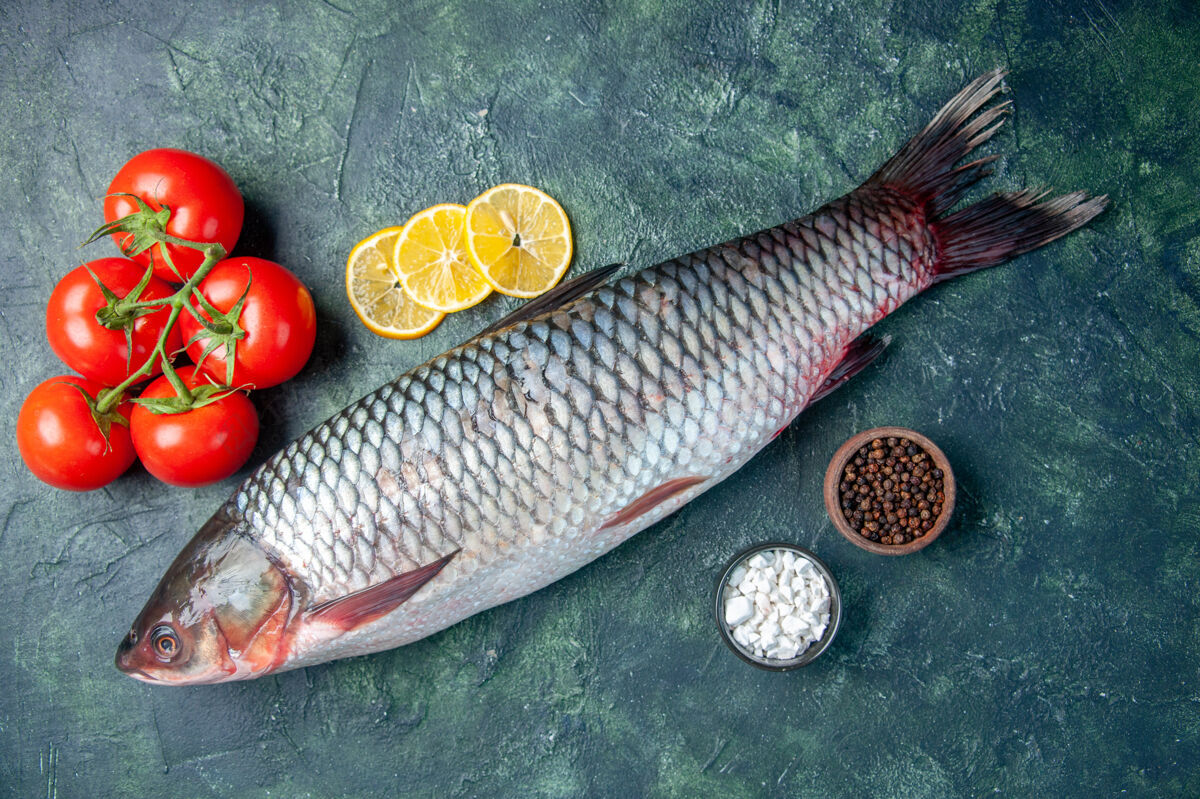 番茄顶视图新鲜的生鱼片与西红柿和柠檬片在深蓝色的背景深色水平蓝色
