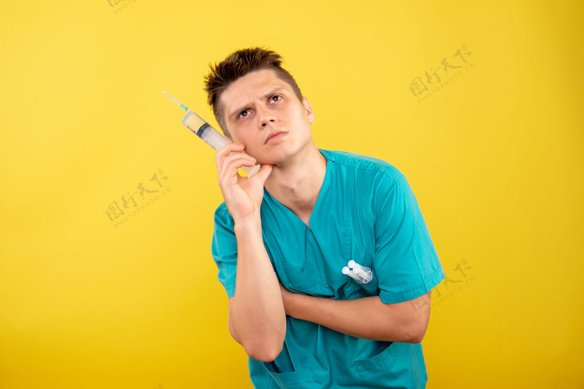健康身穿医疗服的男医生手持针剂 在黄墙上思考男医生套装微笑