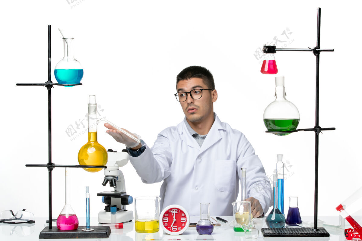 解决方案正面图身着白色医疗服的男性化学家坐在白色背景上 用不同的溶液研究病毒科学实验室的病毒大流行套装医院病毒
