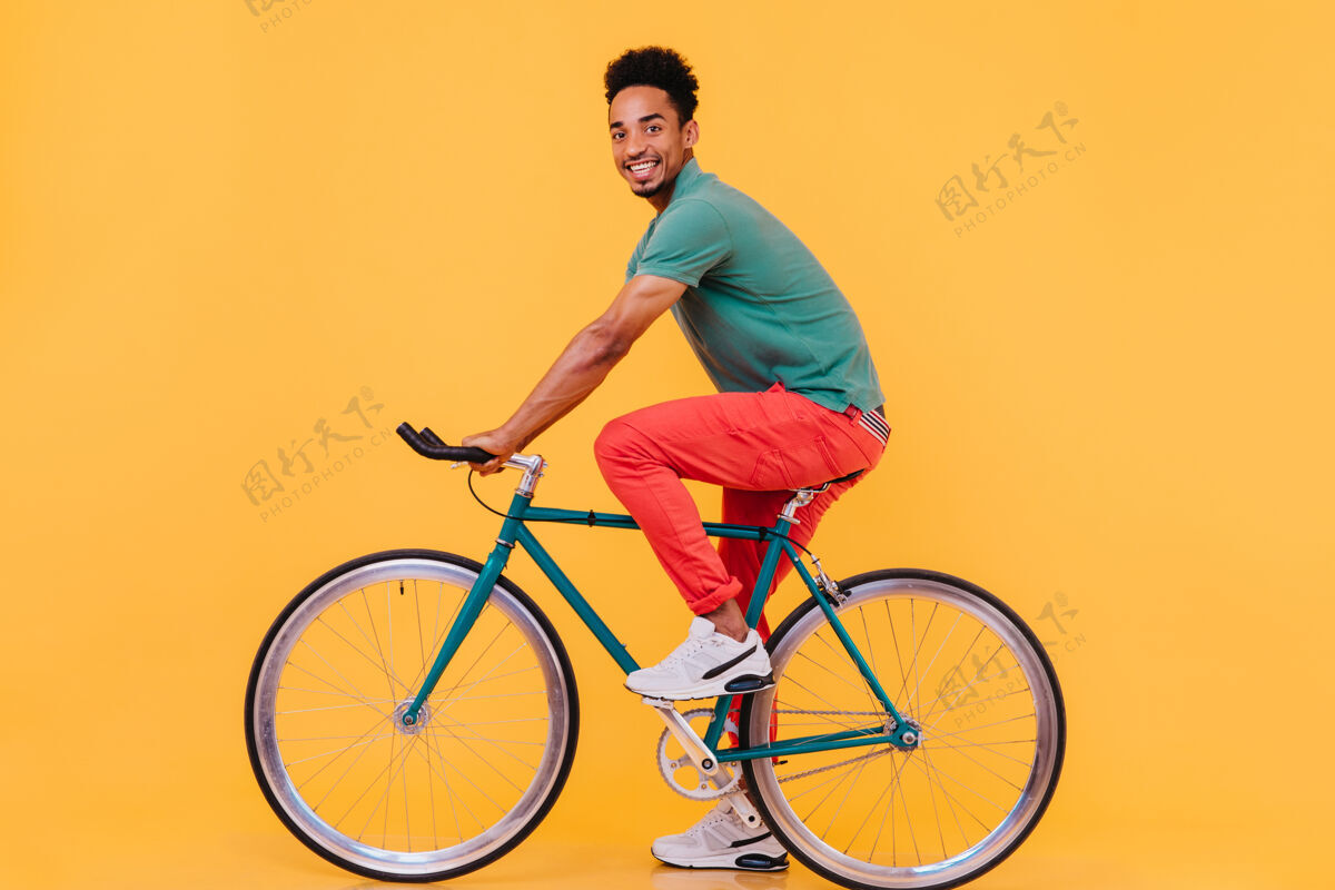 笑穿着运动白鞋的兴奋男模特在自行车上摆姿势欢快的非洲小伙子坐在自行车上看的室内照片表情休闲放松