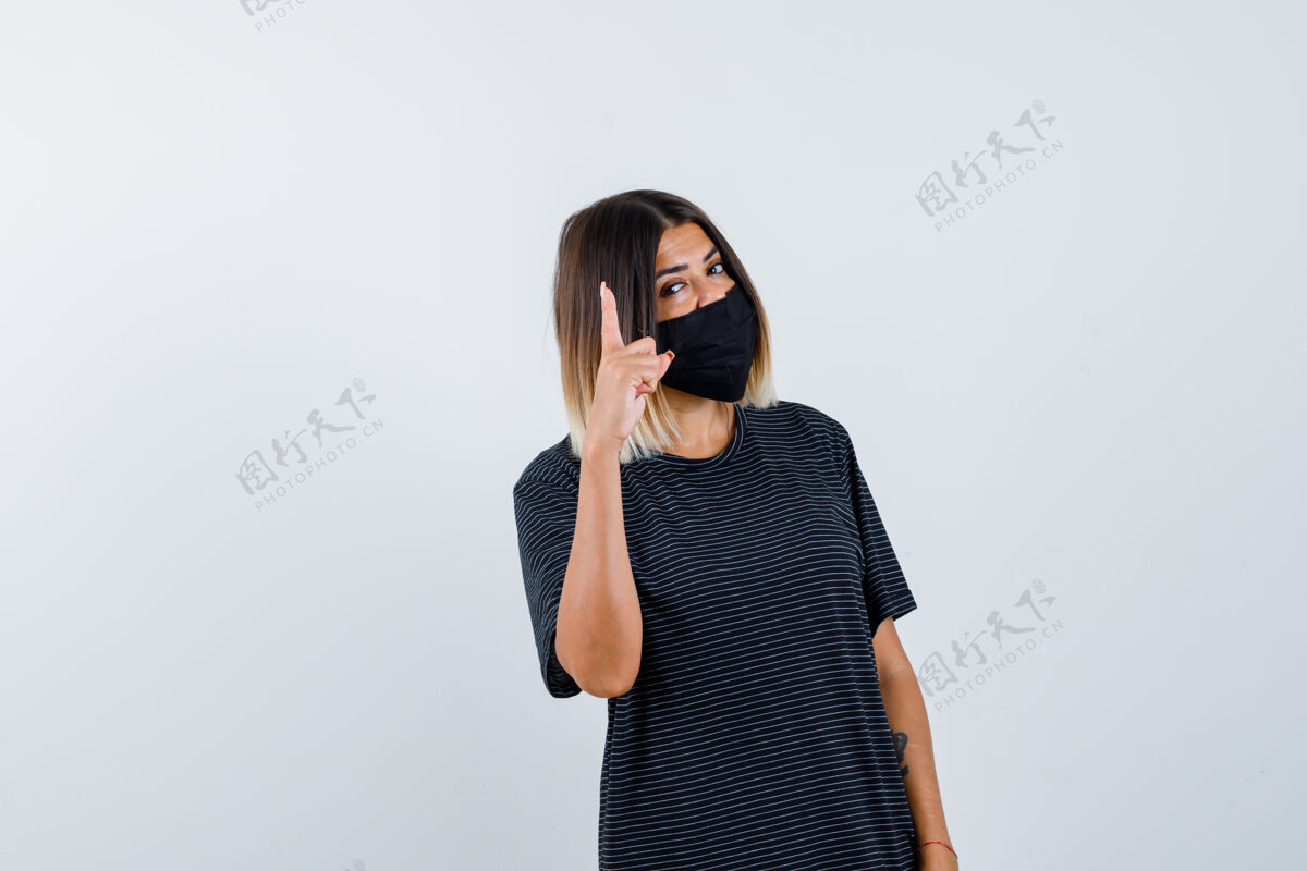 女性身穿黑色连衣裙 戴着黑色面具 表情严肃的年轻女子保持着一个微小的姿势前视图手势显示成人