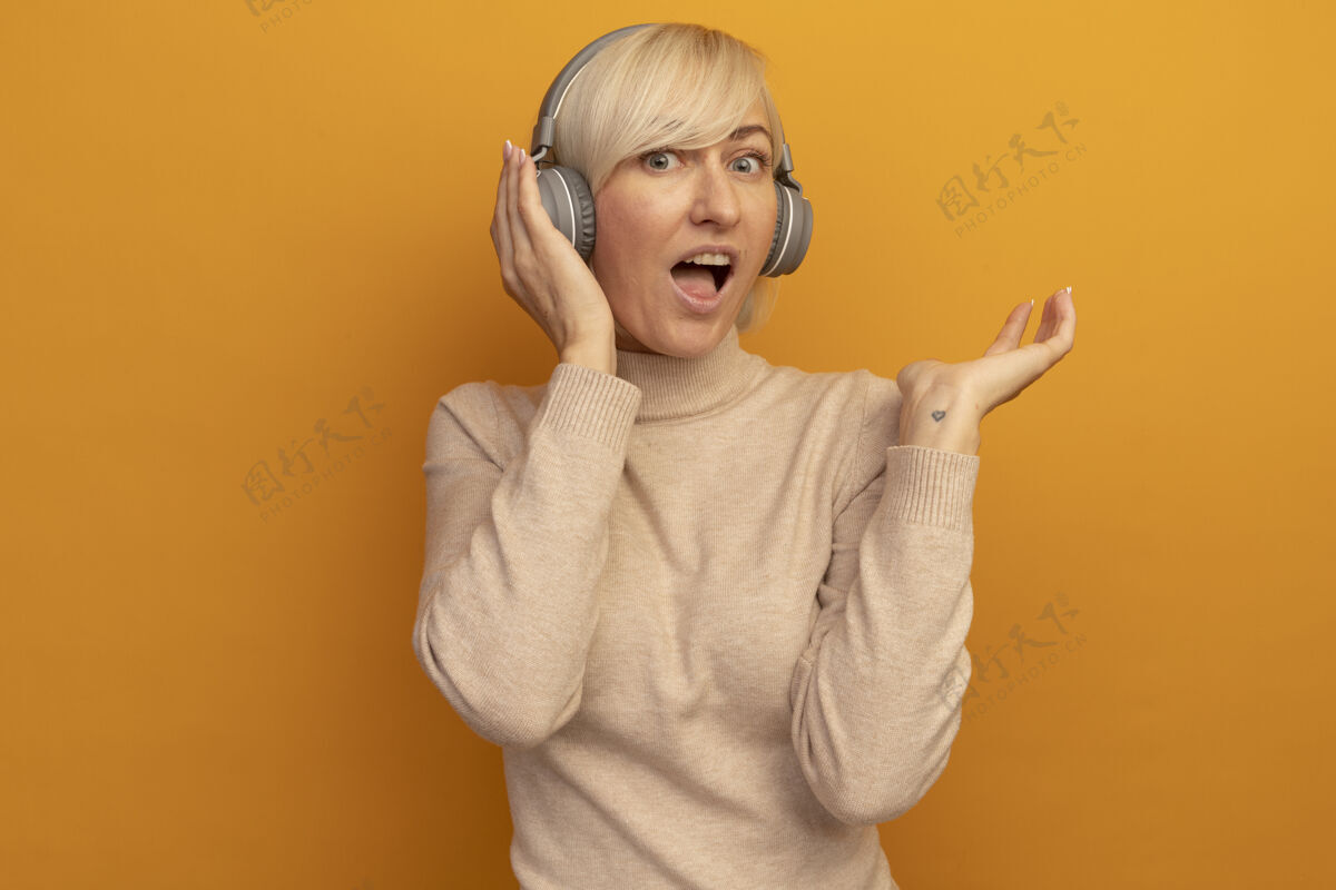 漂亮兴奋的金发斯拉夫女人戴着耳机站着 手张开放在橘子上站着兴奋女人