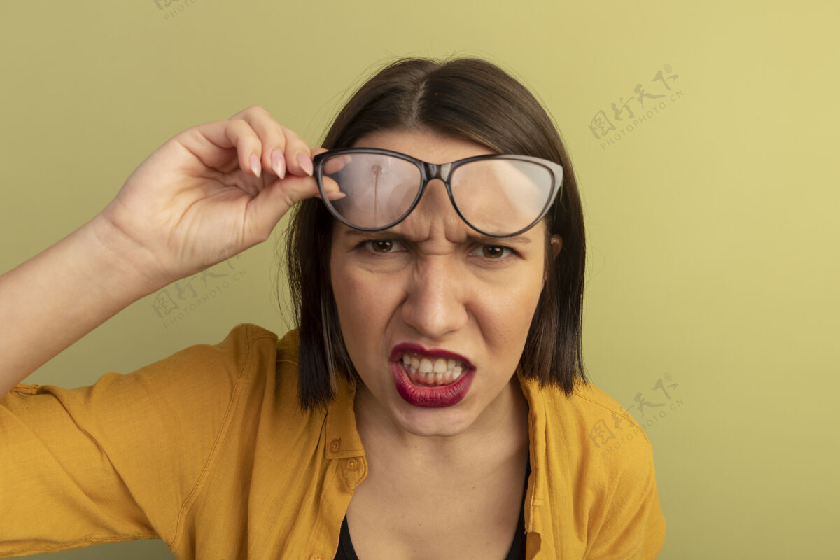 眼镜恼怒的白种女人拿着眼镜 看着橄榄绿的相机女人视觉姿势