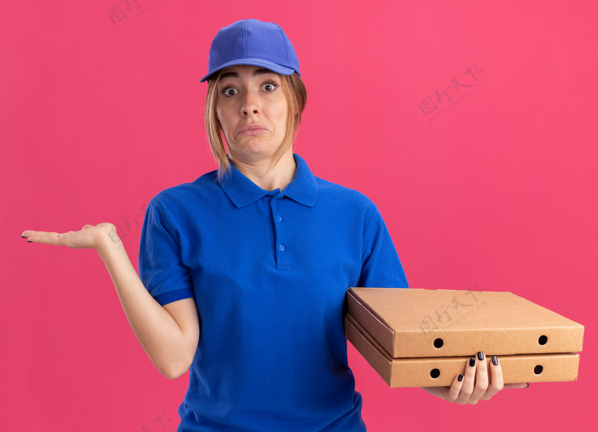 漂亮令人印象深刻的年轻漂亮的送货女孩在制服保持手张开 并持有比萨饼盒粉红色盒子年轻印象