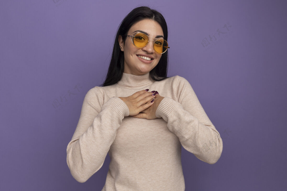 胸部戴着太阳镜的黑发高加索女孩微笑着把手放在紫色的胸前年轻时尚时尚