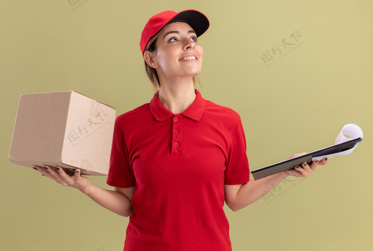 制服微笑着的年轻漂亮的送货女孩穿着制服拿着剪贴板和名片盒看着橄榄绿的一面姿势橄榄壁板
