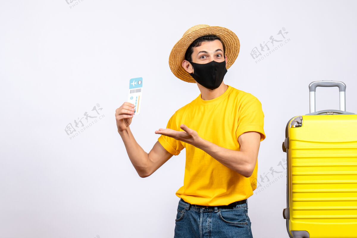 快乐正面图身着黄色t恤的帅哥游客站在黄色手提箱旁举着旅行票手动工具站立手持