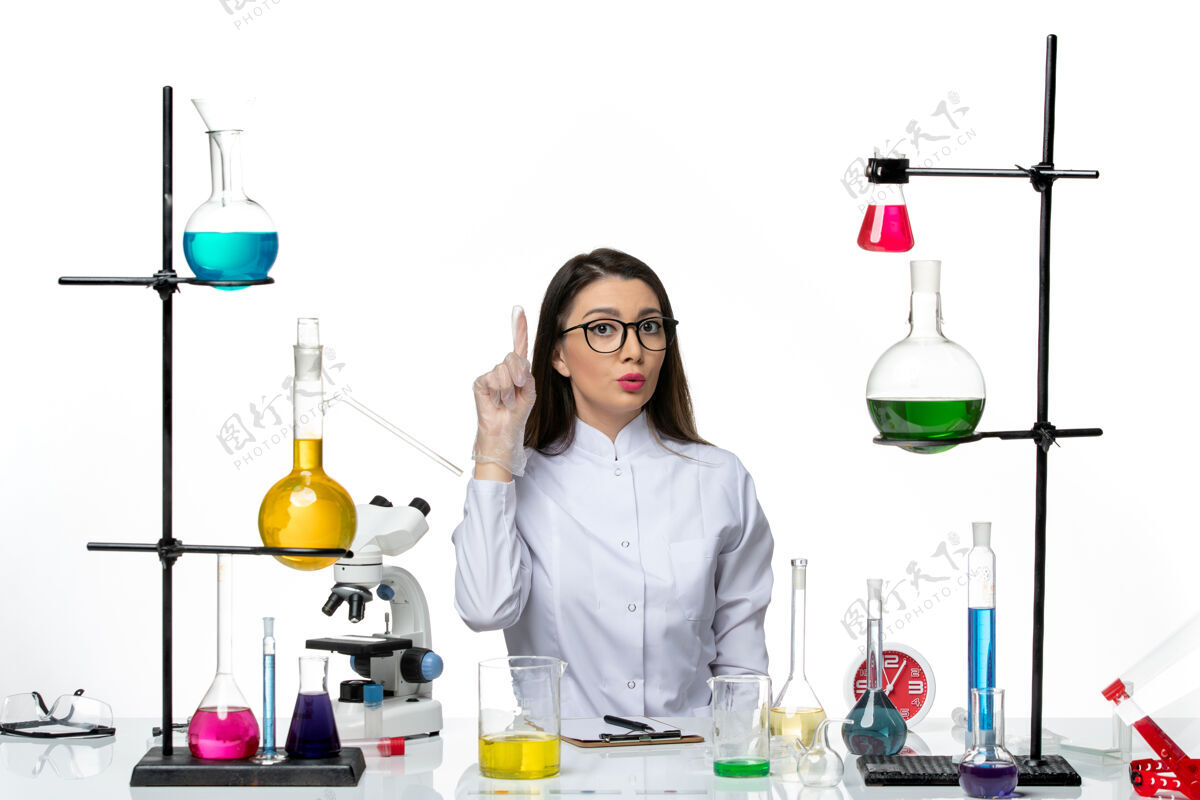 实验室前视图穿着白色医疗服的女化学家坐在白色背景的科学大流行病毒covid实验室里 拿着解决方案葡萄酒药品瓶子