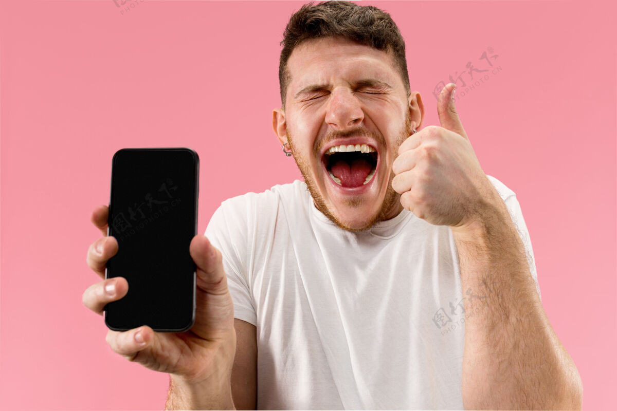抱着年轻帅哥在粉色背景下展示智能手机屏幕 惊喜万分胡须年轻技术