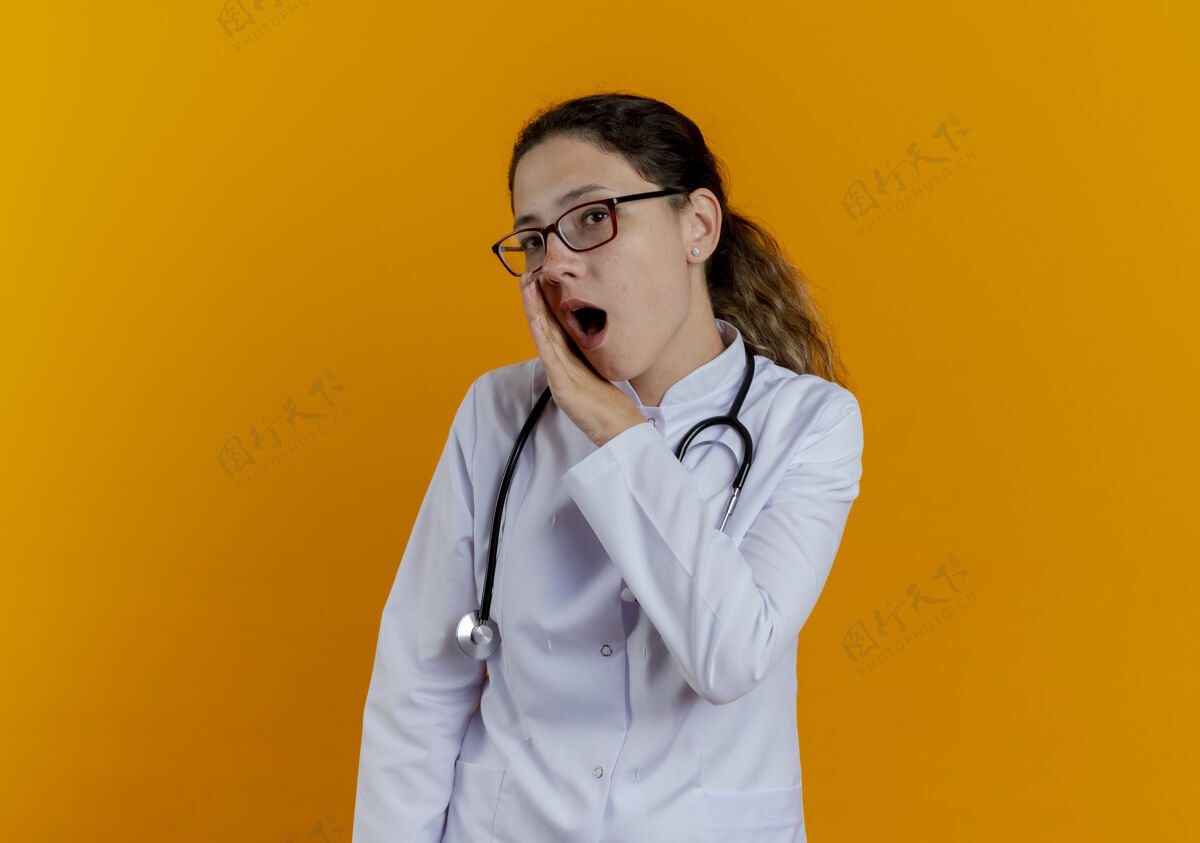 耳语年轻的女医生穿着医用长袍 戴着眼镜听诊器 耳语孤立成年人穿年轻人