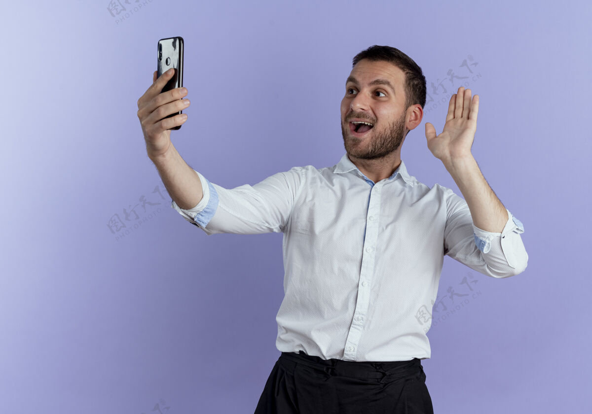 电话快乐的帅哥举起手 看着紫色墙上孤立的电话男人快乐帅气