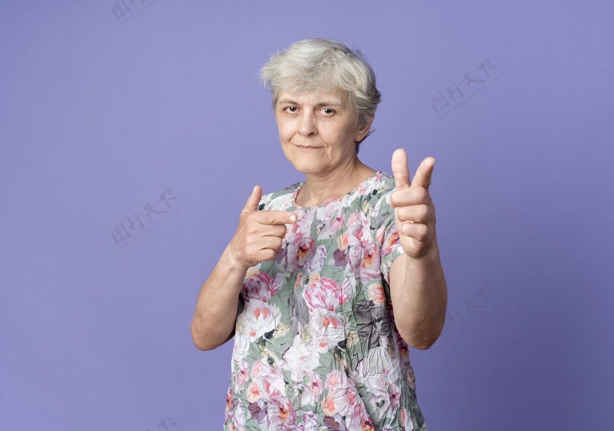 老自信的老妇人双手孤立地指着紫色的墙上二手女人