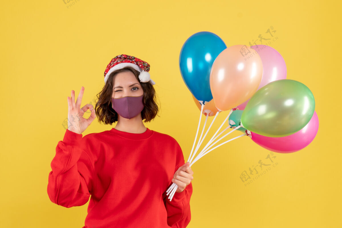 多彩正面图年轻女性手持气球 戴着黄色的无菌面具年聚会乐趣