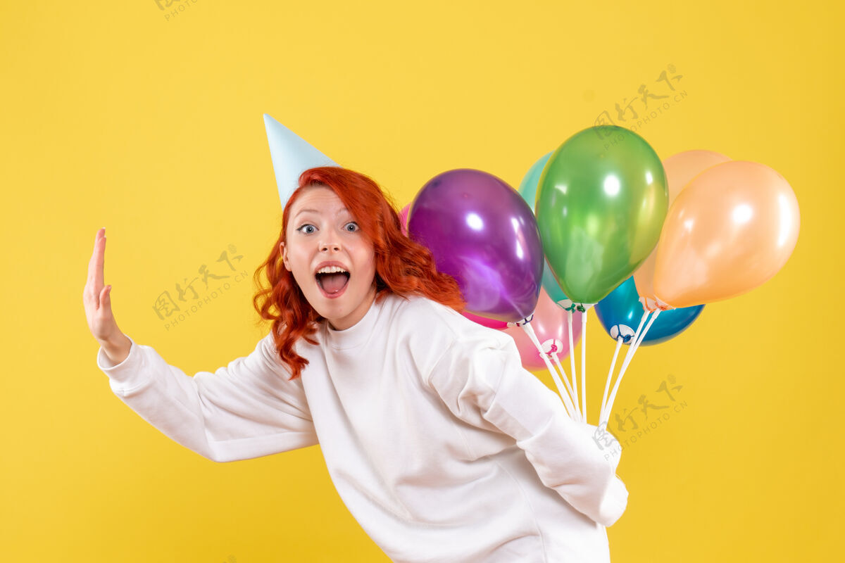 黄色正面图年轻女性藏在背后的黄色背景色新年彩色气球隐藏吹庆祝