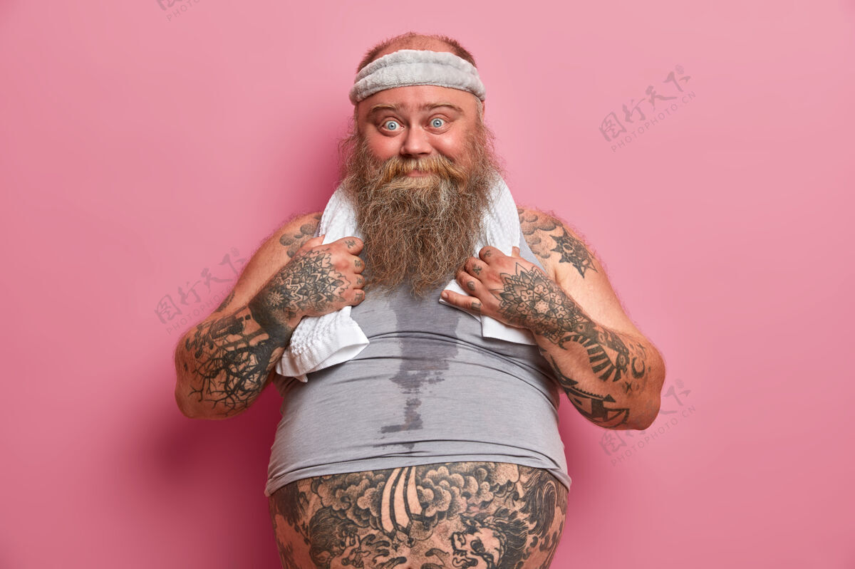 决心有趣的蓝眼睛男人的照片有大肚子 纹身的身体 忙着做健身运动 吃快餐后燃烧卡路里 隔离在粉红色的墙上大个子男人过着健康的生活胡须有氧超重