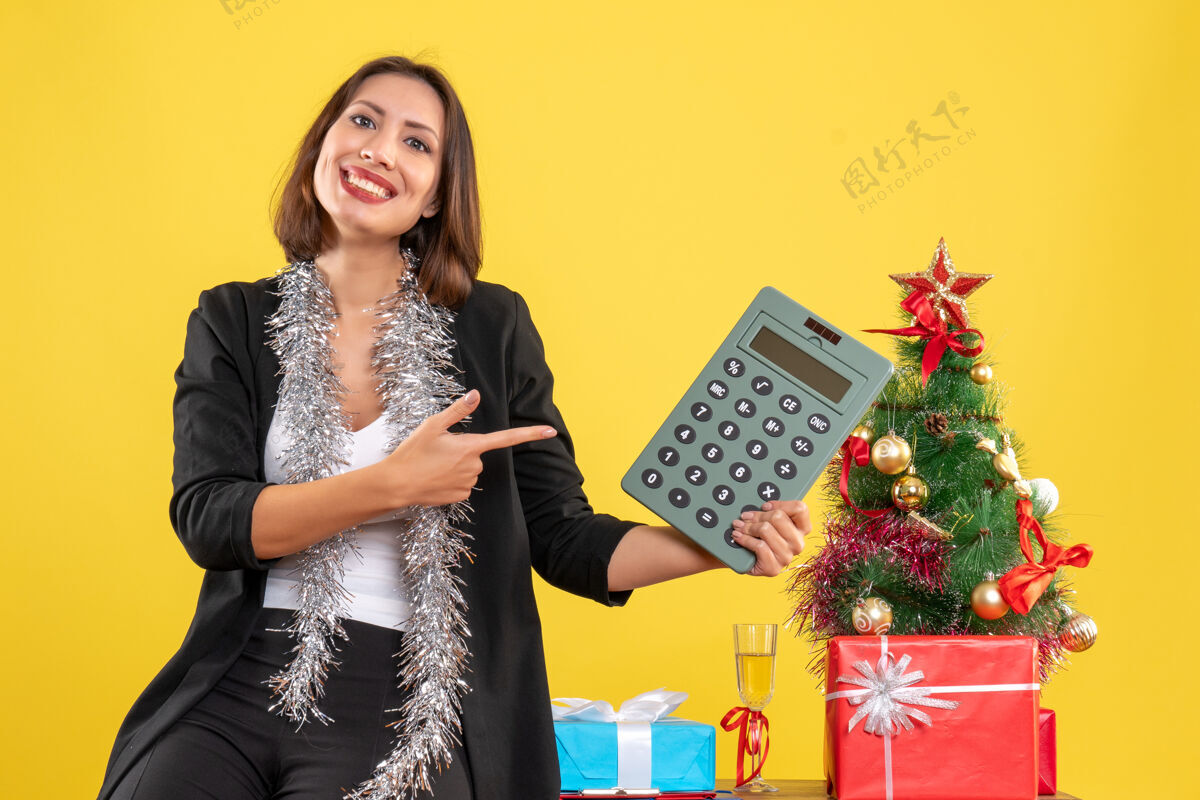 电脑圣诞气氛 微笑的美丽女士站在办公室 指着黄色的办公室计算器微笑计算器美女