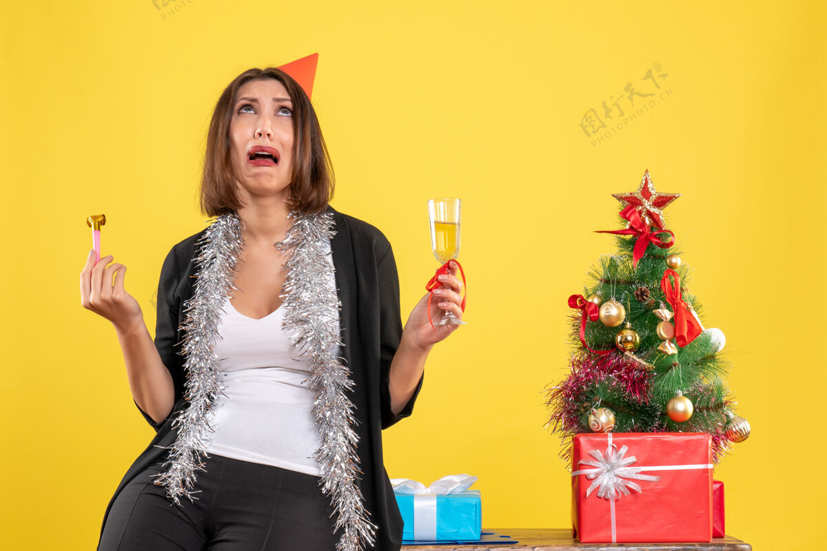 女士圣诞节的心情和害怕美丽的女士拿着酒 在黄色的办公室抬头看人美丽的女士时尚