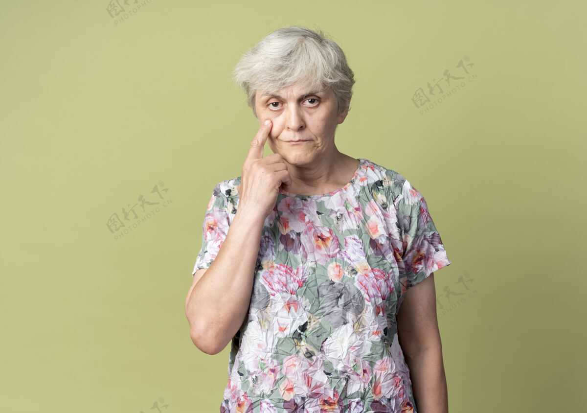 绿自信的老妇人指着橄榄绿墙上孤立的眼睛橄榄自信女人
