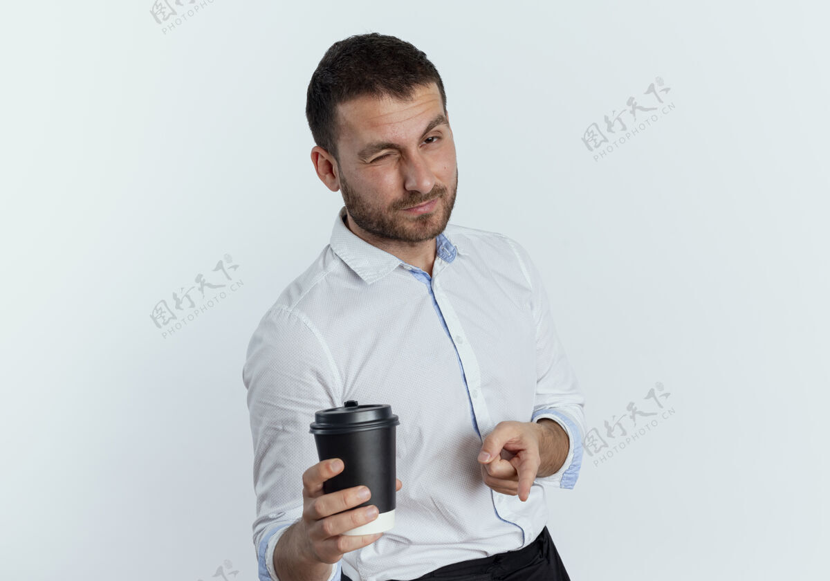 杯子自信的帅哥拿着咖啡杯 孤立地指着白墙上眨着眼睛男人拿着优雅