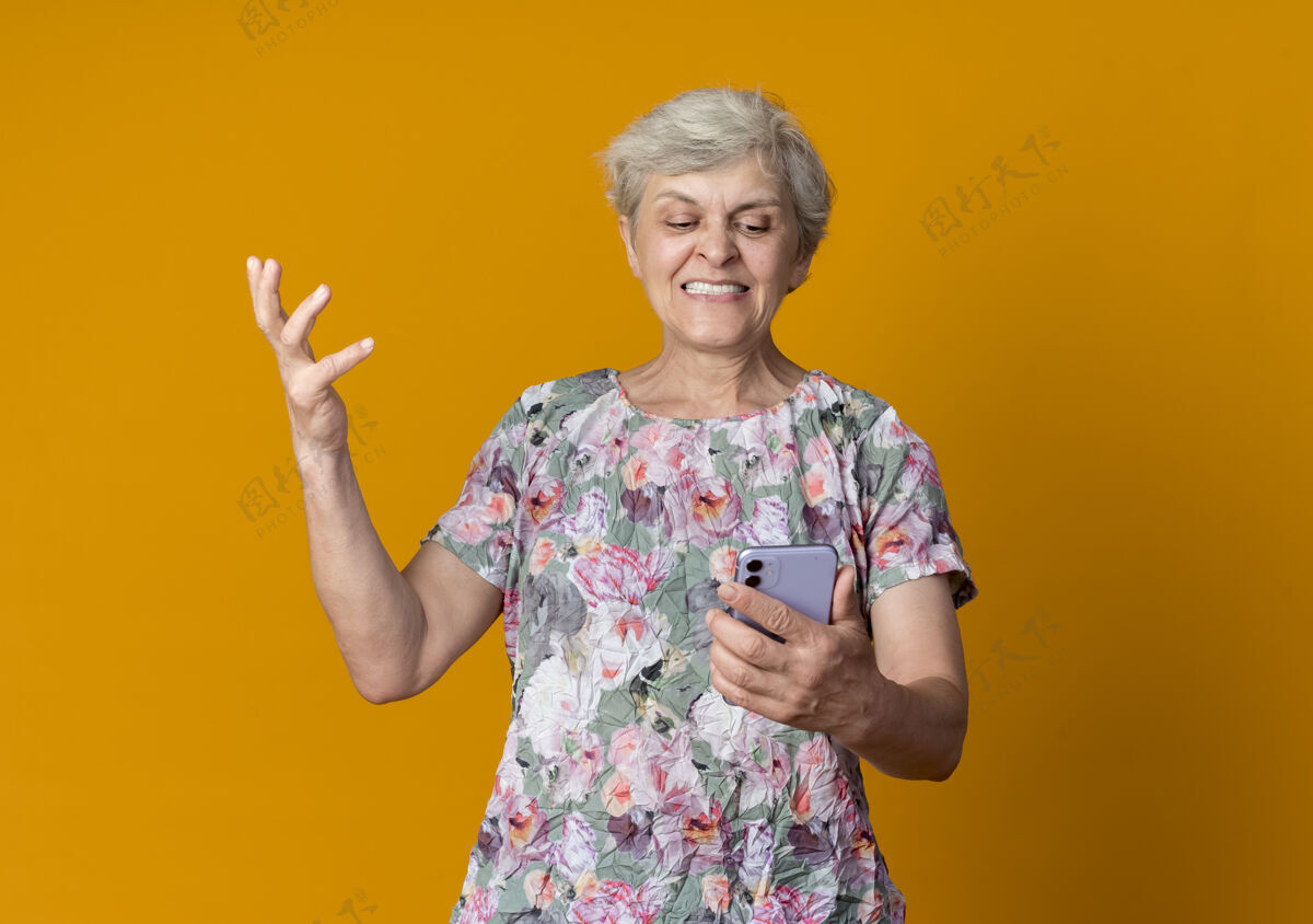 不高兴不高兴的老妇人举起手来 看着隔离在橙色墙上的电话电话手抱着