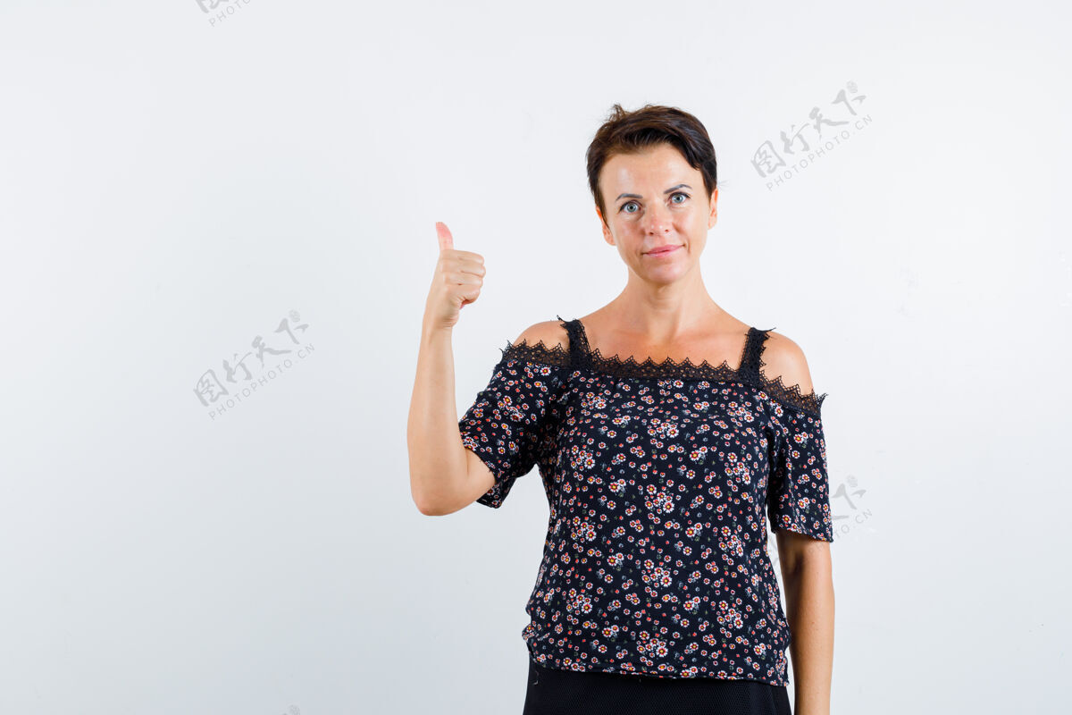 健康成熟的女人在花衬衫 黑色裙子和拇指向上显示自信前视图肖像女性微笑