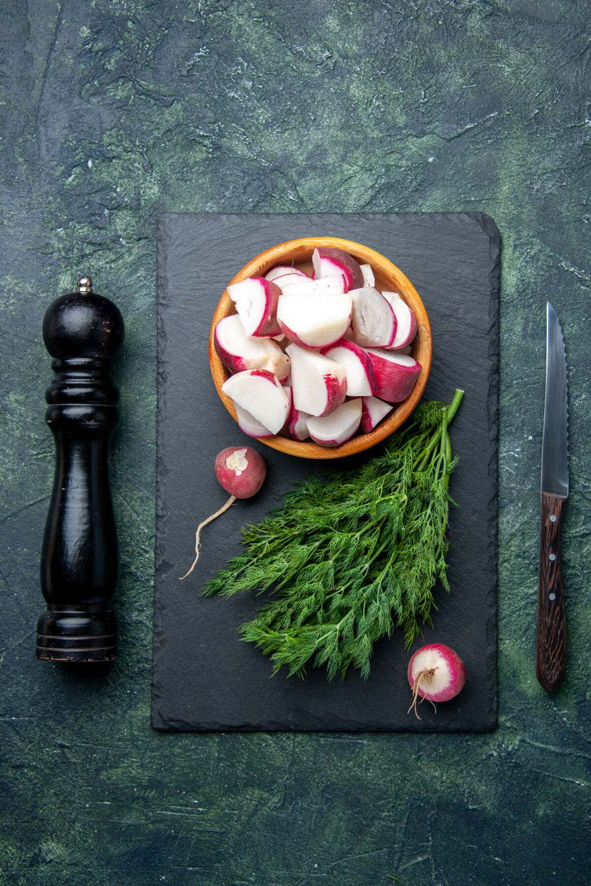 刀新鲜莳萝包和整个切碎的萝卜在黑色砧板上的顶视图厨房锤子刀在混合色背景上 有自由空间生的切割剁碎