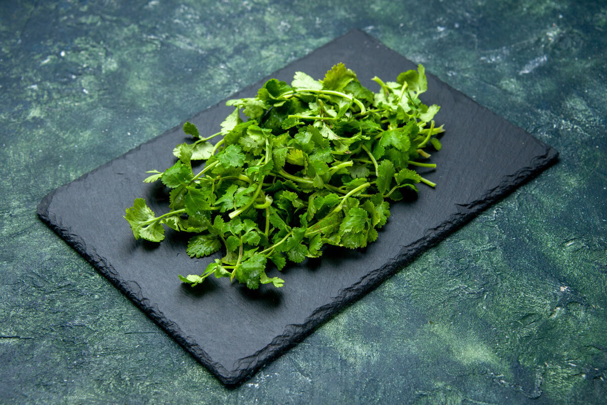 板侧视图的香菜捆绑在木砧板上的绿色和黑色混合色背景与自由空间膳食蔬菜绿色