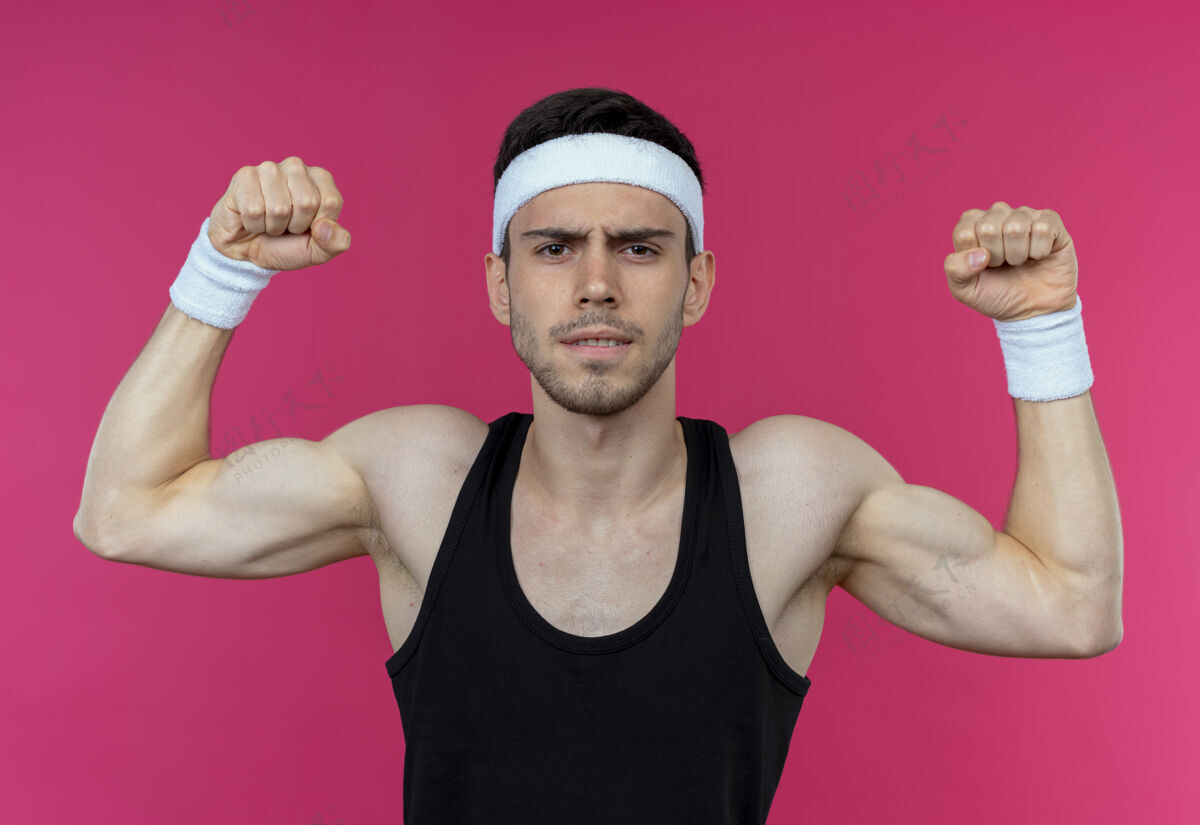 运动戴着头巾的年轻运动型男子 看起来紧张地举起拳头 像站在粉色背景上的athlet头带拳头运动员