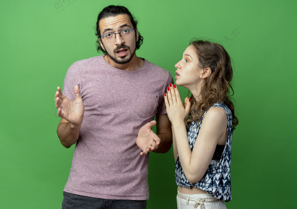手一对年轻的男女 困惑的男人看着镜头 而他的女朋友带着希望的表情问他 双手一起站在绿色的背景上年轻情侣表情