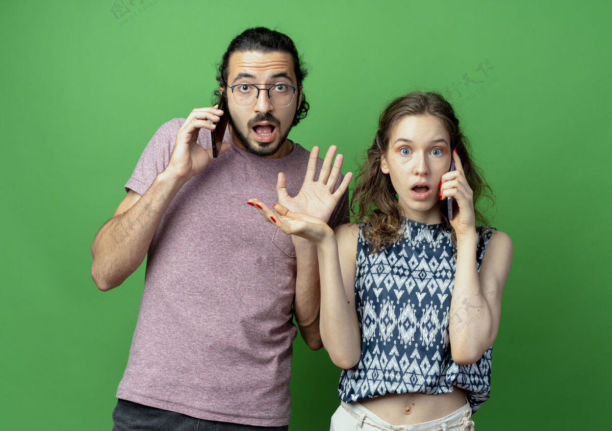 情侣一对年轻夫妇站在绿色的背景下讲手机 感到震惊和失望手机而年轻