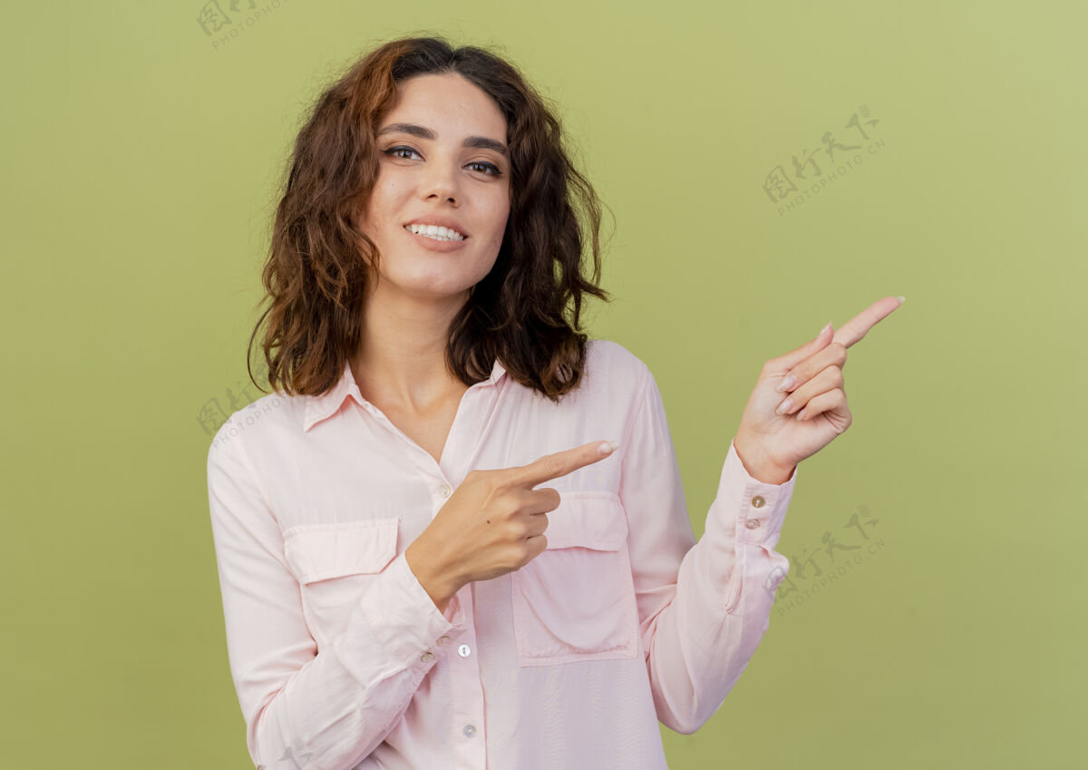 空间年轻的白人女孩微笑着用两只手指着侧面 看着隔离在绿色背景和复印空间的相机微笑壁板绿色