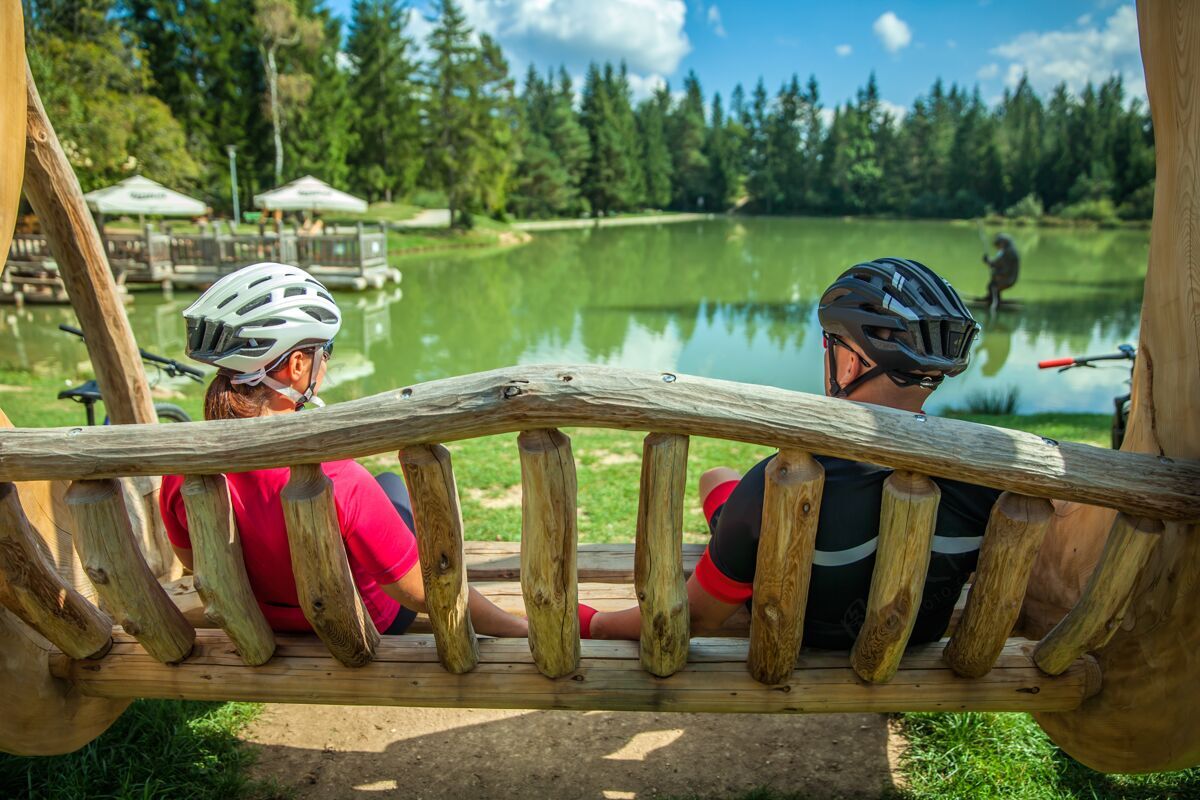 女人一对骑自行车的夫妇在湖边的一个木制秋千上休息快乐湖自行车手