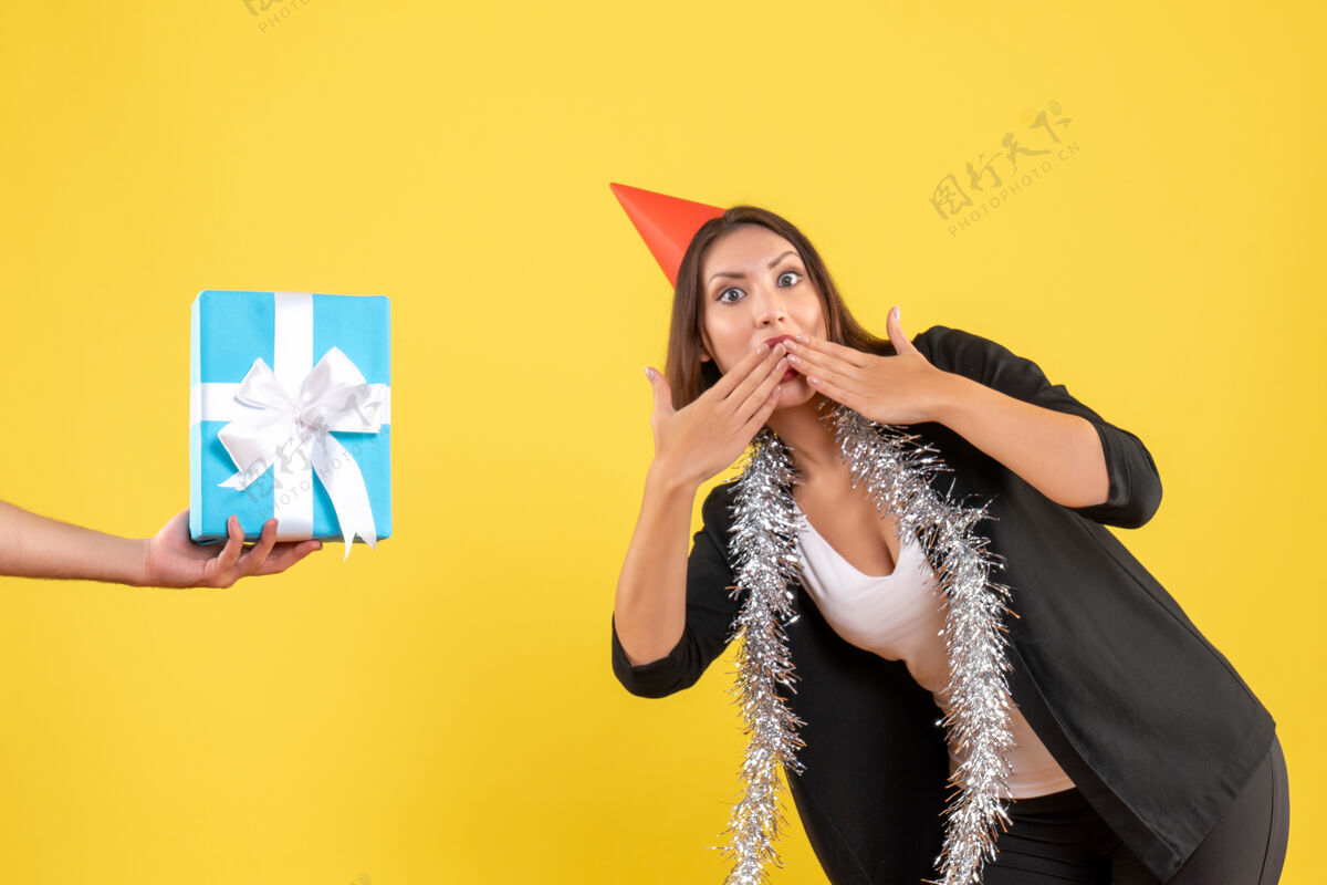 时尚圣诞气氛与惊喜的商务女士在西服与圣诞节帽子和手持礼物的黄色举行公主人