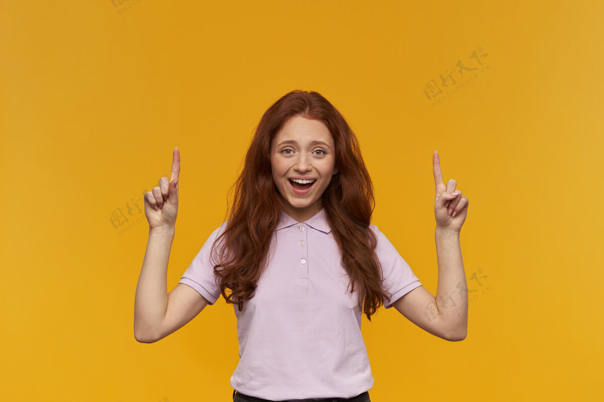 20多岁可爱 快乐的女人 长着姜黄色的头发穿着粉色的t恤情绪概念面带微笑 用食指指着复印空间被隔离在橙色的墙上年轻宽面部