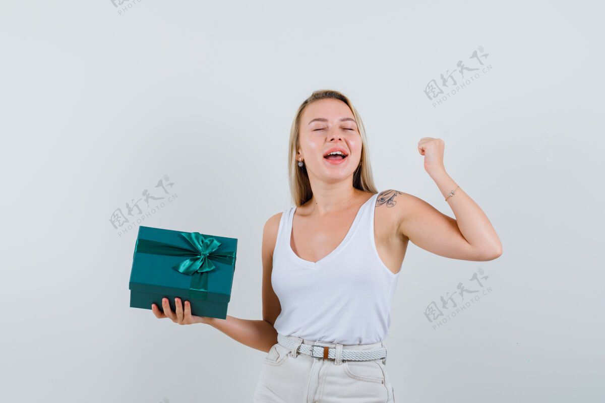 裤子金发女士拿着礼物盒在单身 裤子和看起来幸福 前视图持有年轻盒子