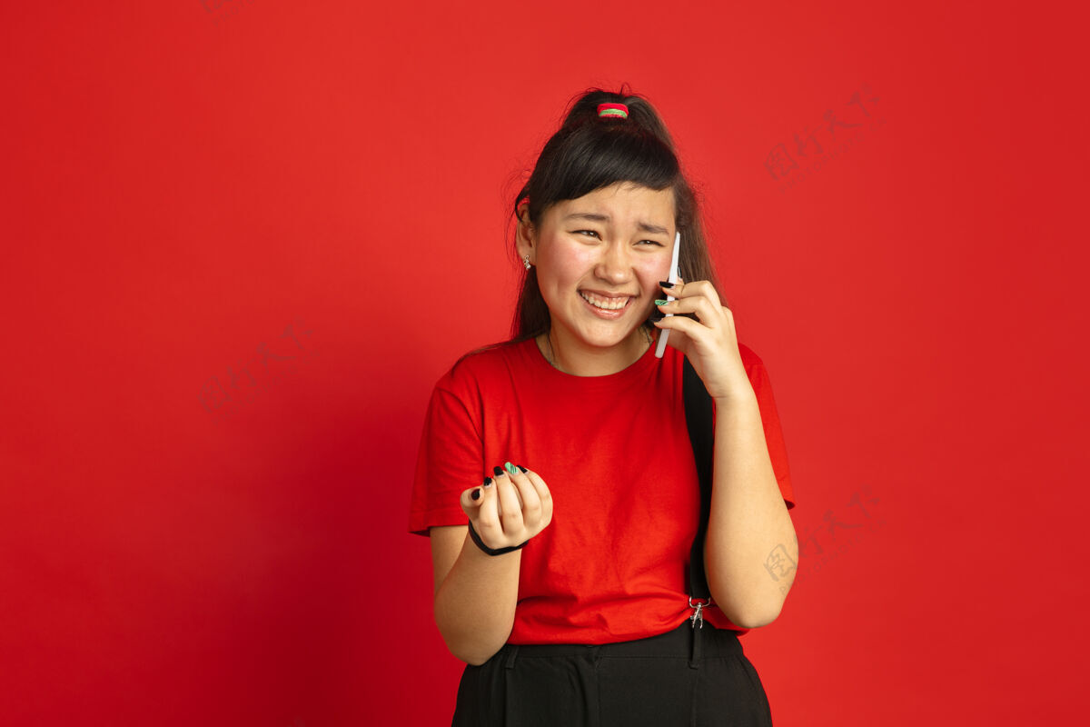 公司在红色工作室背景上孤立的亚洲青少年肖像美丽的深褐色女性模特 随意的长发人类情感的概念 面部表情 销售 广告电话交谈表情工作女性