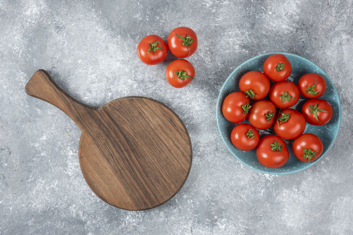 砧板蓝色的碗里装满了红色的新鲜西红柿放在大理石上美味有机蔬菜
