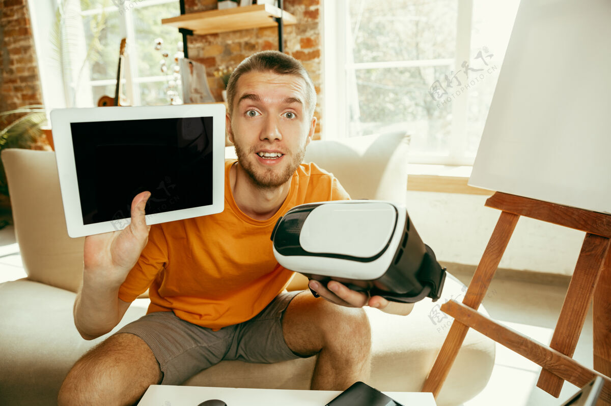记录年轻的白人男性博主 带着专业设备 在家里录制虚拟现实眼镜的视频评论视频博客 虚拟博客男人在流媒体直播时展示虚拟现实的平板电脑和耳机内容直播成人