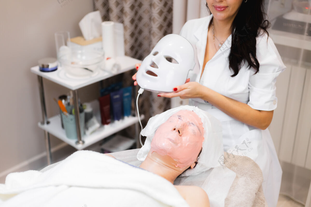 女人客户躺在美容桌上的沙龙里 脸上戴着白色的面具手皮肤护理